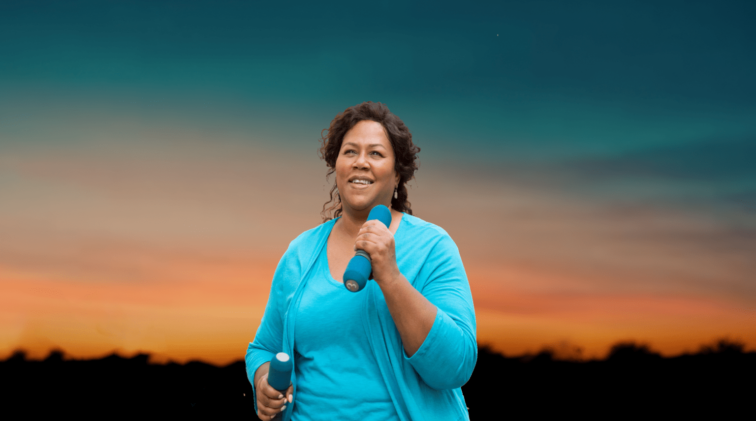 Banner-image-of-a-middle-aged-woman-enthusiastically-walking-outdoors-with-a-pair-of-light-weights-in-her-hands